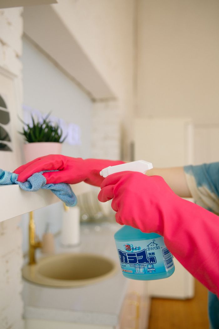 Cleaner in pink gloves spraying and wiping down a kitchen counter