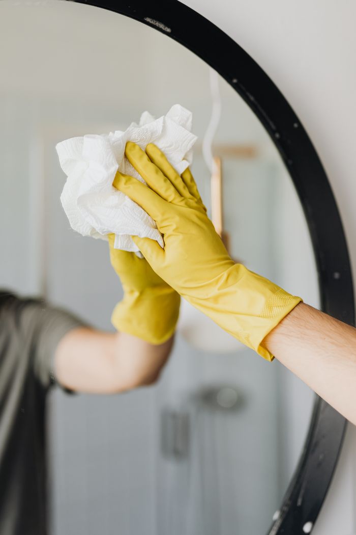 Cleaner wiping a round bathroom mirror with a paper towel
