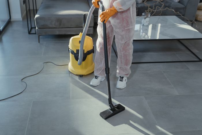 Cleaner in protective coveralls vacuuming a modern living room floor
